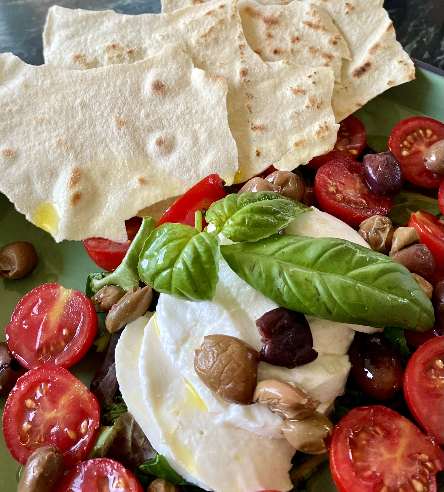 Burrata, tomates cerises, olives, basilic et carasau sur une assiette